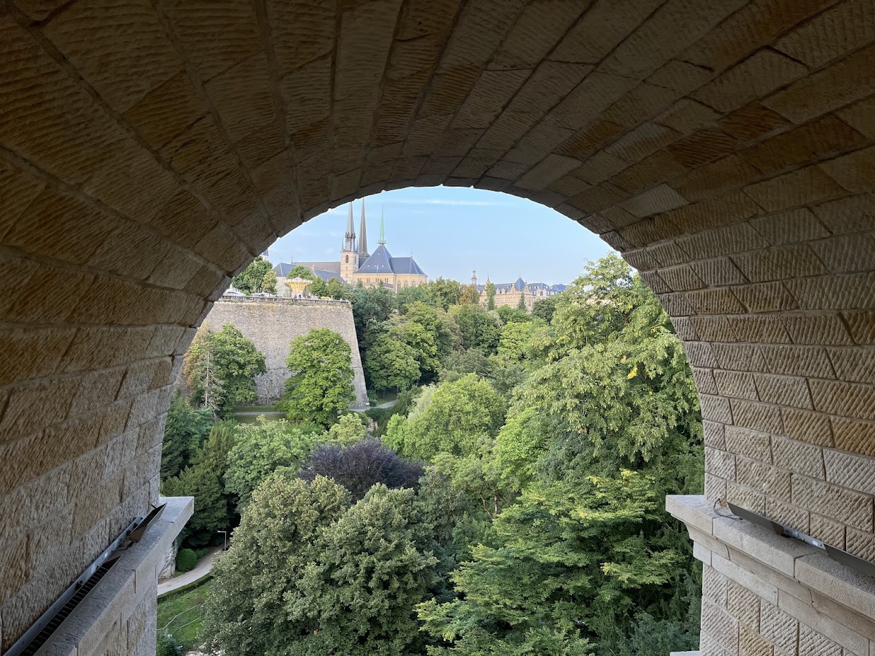 View from the pedestrian walkway beneath the arched Adolphe Bridge, with road traffic above across the Pétrusse valley.